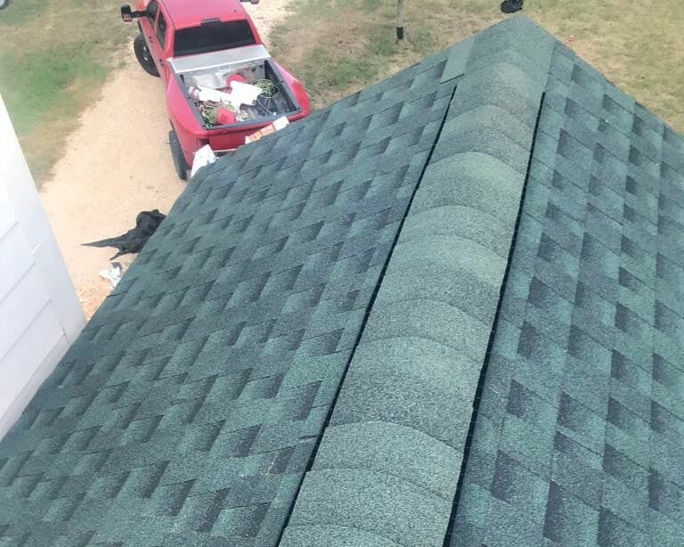 Green shingle roof with red truck in the background.