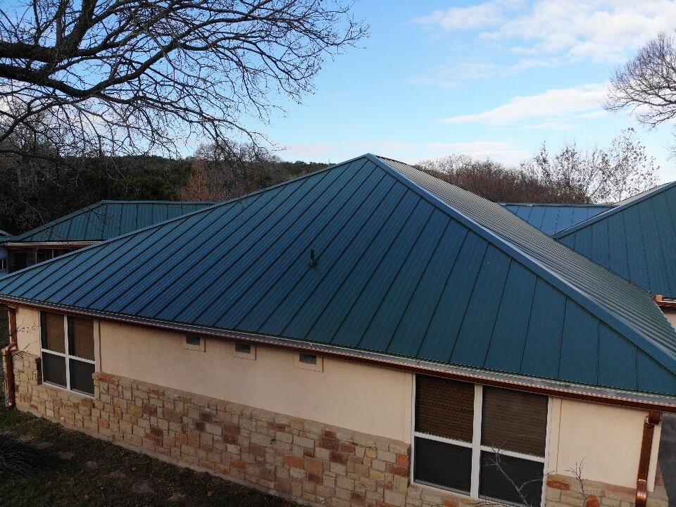 Home in Burnet, Texas with stone exterior and green metal roof installed by A&W Roofing Company.