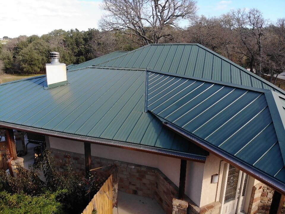 Burnet, Texas home with a green metal roof, a chimney, and a large outdoor space.