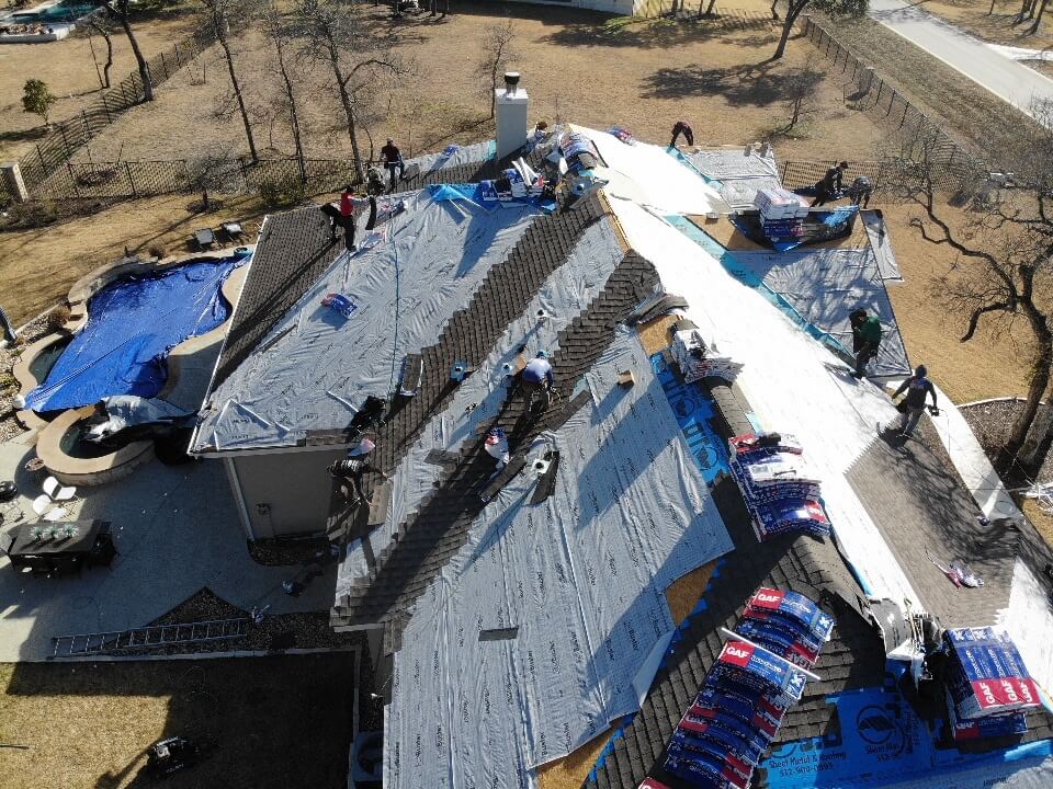 Several construction workers laying down shingles for a re-roof project in Liberty Hill.