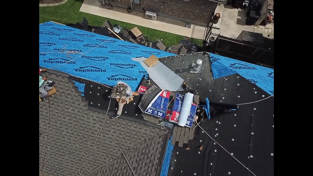 Roof contractor sitting on top of Pflugerville home, nailing down shingles for a new roof installation.