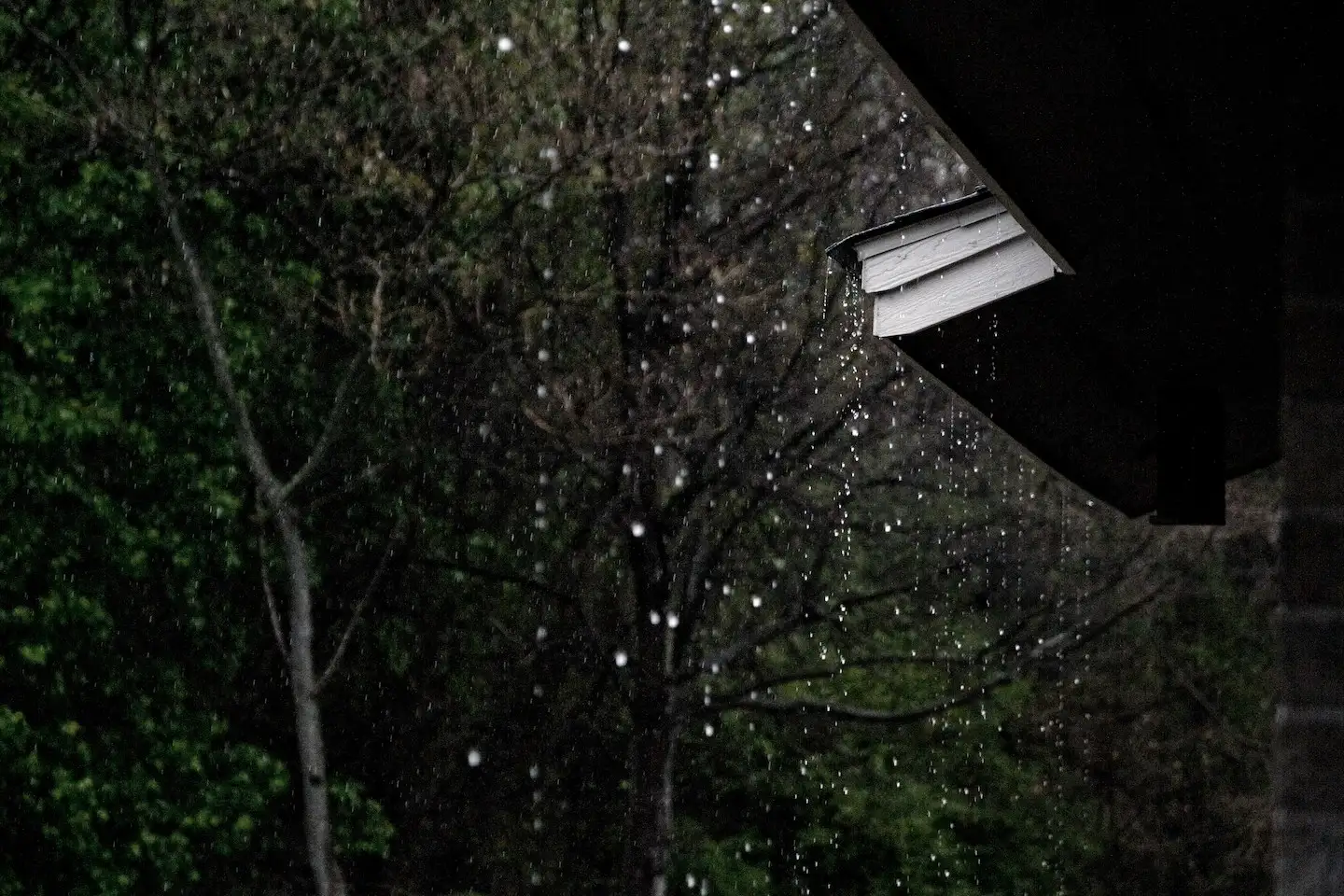 Rain dripping off the corner of a pitched asphalt roof.
