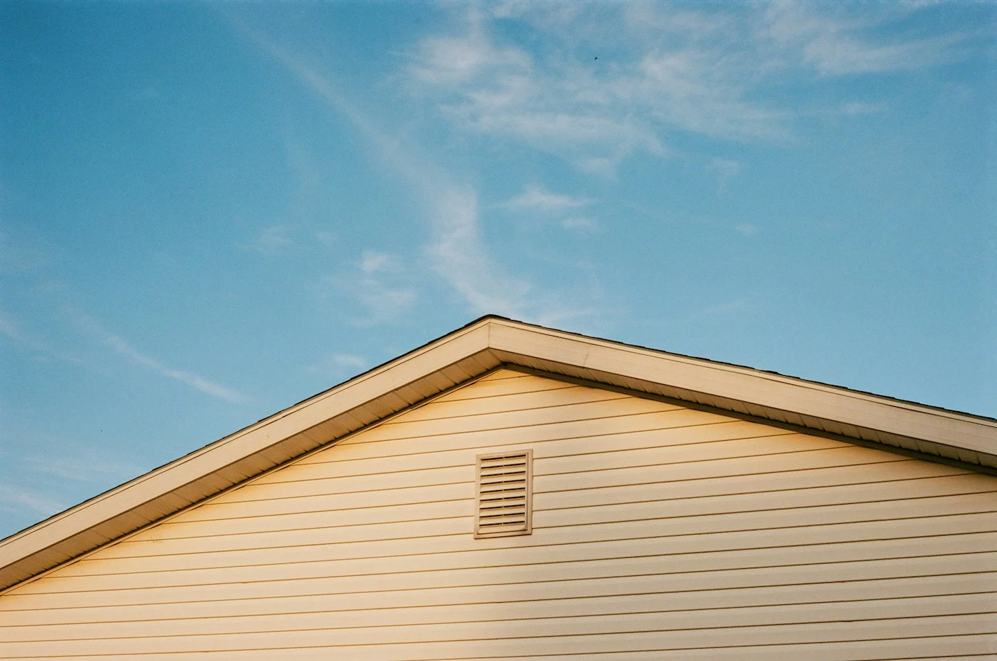 Blue sky with clouds behind the roof of a beige colored home in Georgetown, Texas.

