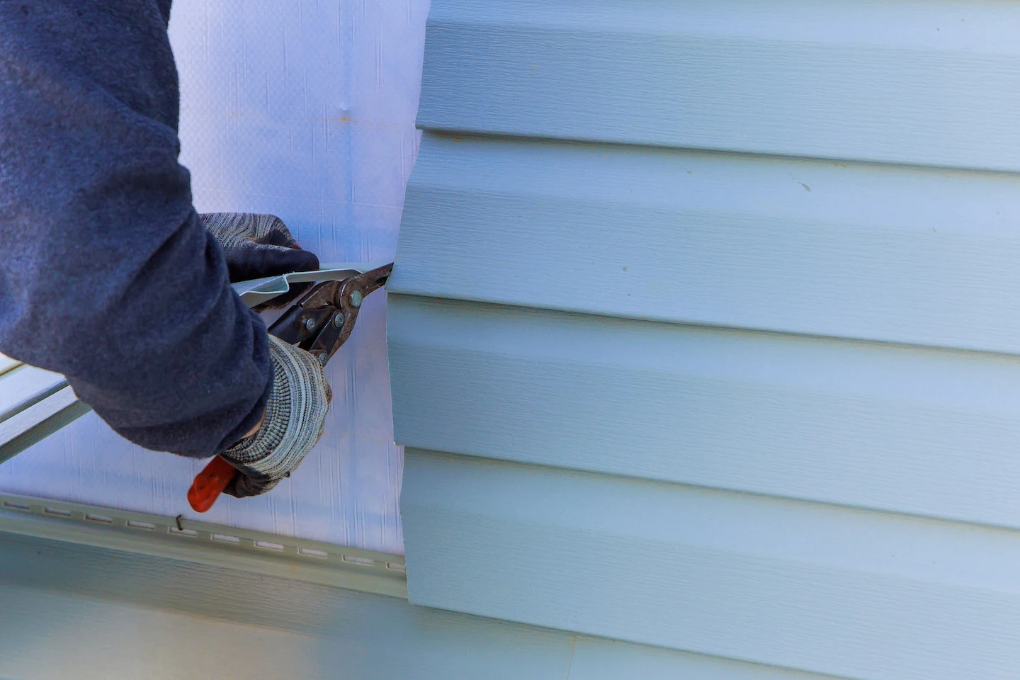 Technician using pliers to install replacement siding panels in Austin.